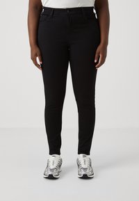 Jeans negros ajustados fabricados con una tela elástica, con un diseño clásico de cinco bolsillos, cierre de cremallera y longitud recta hasta el tobillo. Combinados con zapatillas plateadas.