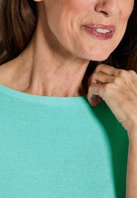 Minzgrüner Strickpullover mit weitem Ausschnitt, der eine feine Textur zeigt. Eine Hand hält sanft den Ausschnitt, was den weichen Stoff hervorhebt.