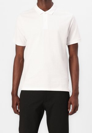Weißes Baumwoll-Polohemd mit Kragen, kurzen Ärmeln und einem einzelnen Knopf am Hals. Mit einem dezenten Logo auf der Brust.