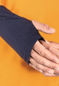 Marinblå långärmad skjorta med tumhål, i kombination med en orange bakgrund. Den texturerade tyget visar lätt stretch och hållbarhet.