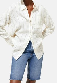 Hvid linned skjorte med knaplukning og fine lodrette striber, lomme detaljer, og en afslappet pasform, parret med mørk denim shorts.