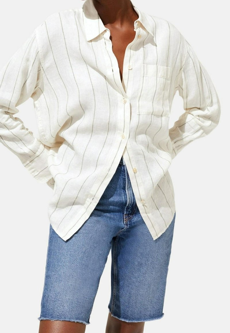 Hvid linned skjorte med knaplukning og fine lodrette striber, lomme detaljer, og en afslappet pasform, parret med mørk denim shorts.