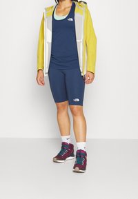 Athletic outfit featuring a yellow and gray jacket, navy tank top, navy shorts, and maroon sneakers with teal accents and white socks.