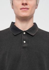 Black polo shirt made of cotton, featuring a collar, two buttons, and a textured surface. Simple design with a relaxed fit.