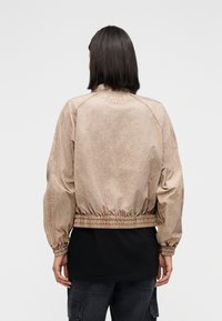 Μπεζ μπο υφάν bomber με υφασμάτινη υφή, ελαστική μέση και μανίκια με πιέτες. Απλός σχεδιασμός με ουδέτερη χρωματική παλέτα.