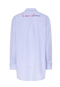 Espalda de una camisa de manga larga a rayas azul claro y blanca con texto bordado en rojo y azul que dice "Ti devi calmare" en la parte superior de la espalda.