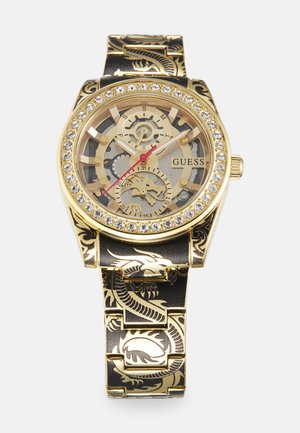 Gold-tone watch with a transparent dial, skeleton design, and red accents. Black strap features embossed dragon pattern and gold detailing.