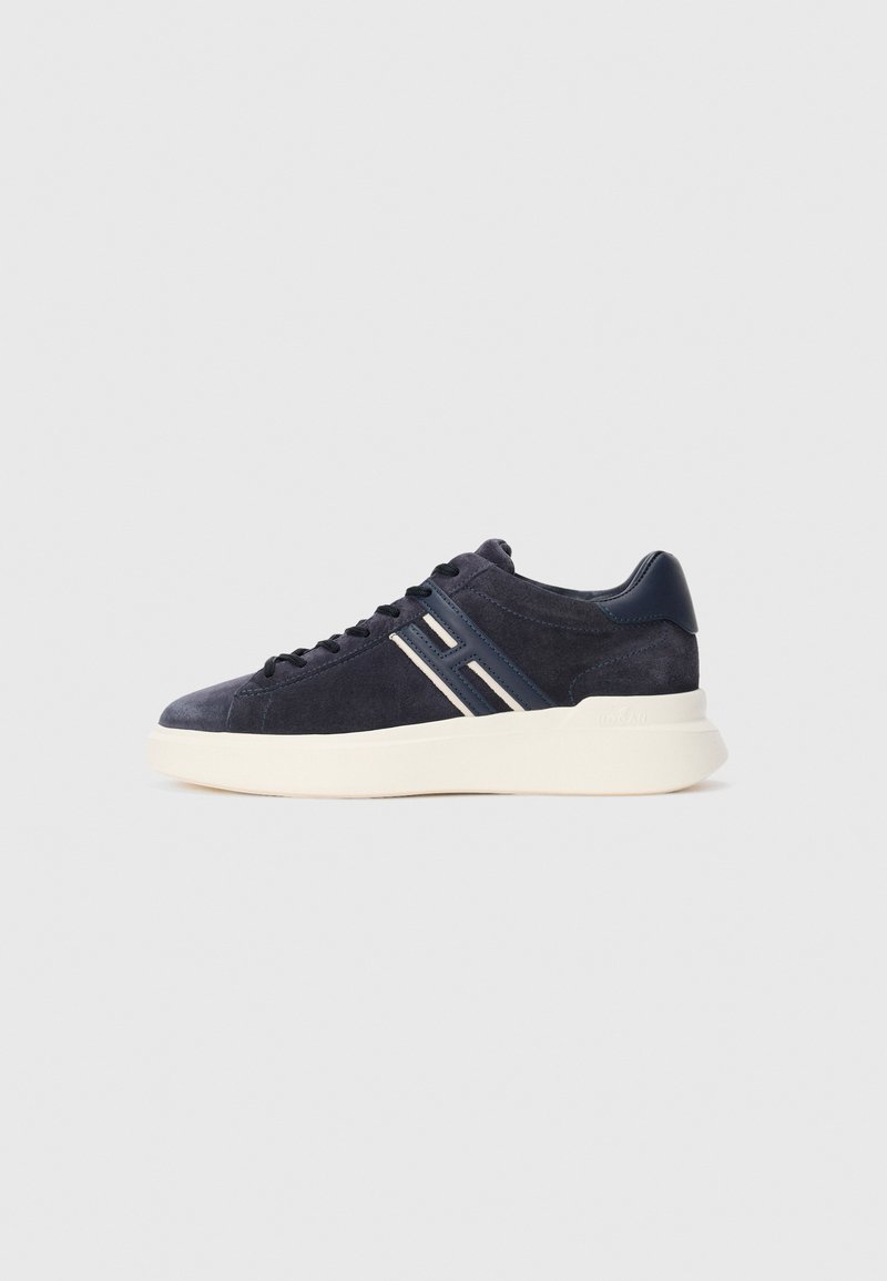Navy blue suede sneaker with black laces, white sole, and white and navy striped "H" detail on the side.