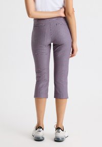 Pantalones Capri en un patrón de cuadros morado y blanco, con cintura a media altura, que cuentan con bolsillos traseros y se combinan con zapatillas deportivas blancas.
