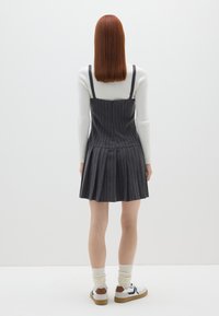 Vestido de rayas en gris oscuro, sin mangas, con un corsé ajustado y falda acampanada. Combinado con zapatillas blancas y calcetines crew en color crema.