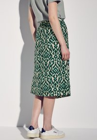 Grön mönstrad kjol med dragsko i midjan, knälång, med ett geometriskt mönster och matchad med vita sneakers.