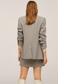 Checked blazer with wide lapels and rolled sleeves, paired with a matching skirt. Color scheme features gray, black, and white.