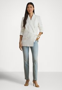 Balts, divrindu linu žakete ar piegriezumu, kombinēts ar gaiši zilām taisnajām džinsi kājām un zelta ādas siksniņu augstpapēžu sandales.