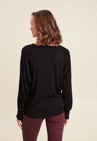 Schwarzer Pullover mit langen Ärmeln, lockerer Passform, gerippten Bündchen und rundem Ausschnitt, kombiniert mit burgunderroten, engen Hosen. Glatte Textur.