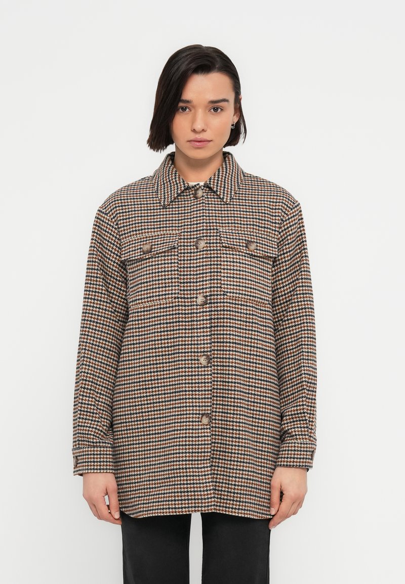 Καρό πουκάμισο-ζακέτα σε καφέ, κρεμ και μαύρο. Διαθέτει γιακά, κουμπιά μπροστά και δύο τσέπες στήθους. Κατασκευασμένο από υφασμάτινη υφή.