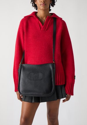 Bolso de hombro de cuero negro con acabado texturizado y herrajes dorados, combinado con un suéter de punto rojo con cuello y puños acanalados.