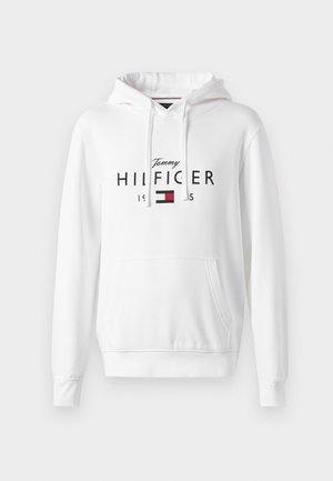 Hvid hættetrøje med lomme foran, der viser "Tommy HILFIGER" logoet i sort og et lille rødt og blåt flagdesign. Blødt stof tekstur.