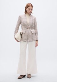 Blazer en tweed texturé à la taille cintrée, nuances de rose clair et blanc ; associé à un pantalon large crème et un sac beige.