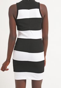 Vestido sin mangas a rayas en blanco y negro con forma ajustada, que presenta un cuello alto y una cremallera en la parte posterior.
