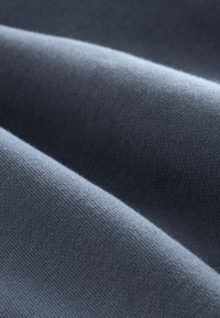 Donkerblauwe stof met een zachte, gladde textuur, voorzien van fijngebreid materiaal en subtiele golven, waarmee de val en het gewicht worden benadrukt.