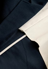 Tessuto stratificato in blu navy e crema, con una texture liscia. La sezione blu navy è più spessa, mentre quella crema è più leggera con un bordo pulito.