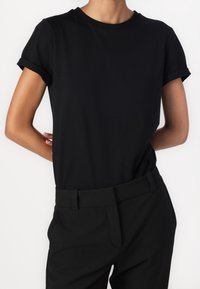 Zwarte katoen t-shirt met korte opgerolde mouwen en een ronde halslijn, gecombineerd met zwarte high-waisted broek met een riem.