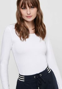 Weißes langärmeliges Oberteil kombiniert mit marineblauen Jogginghosen mit verstellbarem Bund und gestreiftem Elastikband. Glatte Textur, figurbetontes Design. Keine sichtbaren Muster.