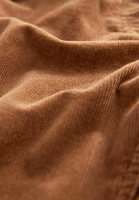 Un tissu en velours côtelé texturé dans une teinte marron chaud, présentant des plis ondulés et de fines côtes verticales qui mettent en valeur sa surface douce et accueillante.