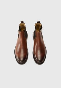 Brown leather chelsea boots with elastic side panels, rounded toe, and contrasting dark accents. Smooth texture and minimal stitching detail.