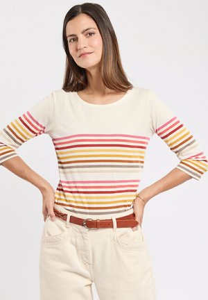 Haut à manches longues crème clair avec des rayures horizontales en rose, orange, jaune et marron. Associé à une ceinture marron et un pantalon beigne.