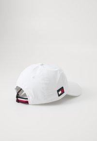 Cappello da baseball bianco con cinturino regolabile, presenta una toppa con il logo in rosso, bianco e blu navy. Tessuto morbido con corona arrotondata e visiera curva.