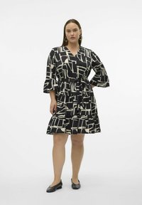 Robe noire et ivoire à motifs avec un décolleté en V, des manches évasées et une taille ceinturée, présentant des volants superposés au niveau de l'ourlet.