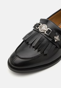 Mustad nahast loafers, millel on fringi disain, dekoratiivne hõbedane riistvara ja detailne õmblusäär, et lisada tekstuuri.