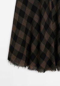 Tissu à carreaux noirs et marron avec un ourlet frangé, drapé sur un fond blanc.