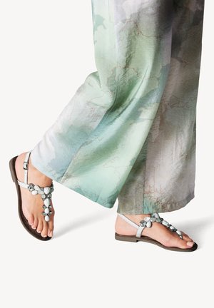 Sandali piatti a strap t di colore blu chiaro in ecopelle, decorati con pietre lisce bianche e grigie, abbinati a pantaloni larghi a motivi di colore verde pallido.
