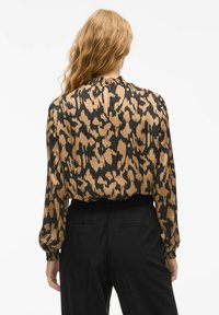 Blusa a maniche lunghe con stampa leopardata marrone e nera, caratterizzata da un colletto arricciato e un'apertura a chiave sul retro, realizzata in tessuto leggero.