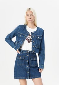 Jeans jakna s skrajšanim krojem in štirimi sprednjimi žepi, v kombinaciji z ujemajočo se jeans krilom, ki ima gumbno zapiranje in dva sprednja žepa.