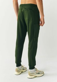 Grüne Jogginghose mit geripptem Bund, seitlichen Taschen und einer Gesäßtasche. Hergestellt aus glattem Stoff, mit entspannter Passform und schmal zulaufenden Beinen.