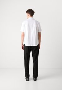 Rövid ujjú fehér ing, klasszikus gallérral, fekete nadrággal párosítva. Simább anyag, klasszikus szabás; minimalista design.