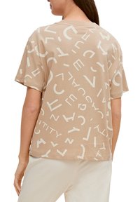 Beige T-shirt lavet af blødt stof, med store, kontrasterende hvide bogstaver i forskellige skrifttyper og størrelser, med en afslappet pasform og korte ærmer.