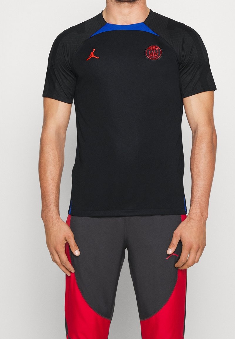 Czarny t-shirt sportowy z niebieskimi akcentami, z czerwonym logo na piersi. Wykonany z materiału odprowadzającego wilgoć, krótki rękaw.