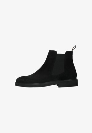 Bottes Chelsea en daim noir avec panneau latéral élastique, languette de tirage au talon et semelle basse empilée, présentées en profil droit sur fond blanc.