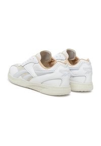 Baltos sportinės bateliai, pagaminti iš odos ir zomšos, su žemu dizainu, perforuotais akcentais ir tekstūriniu guminio pado su dėmėtu paviršiumi.