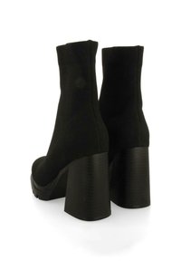 Botas negras de tacón alto con parte superior de tela elástica, suela gruesa estriada y tacones cilíndricos gruesos. Diseño elegante y minimalista con superficie texturizada.