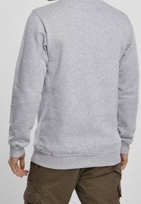 Sudadera gris con escote redondo, puños y dobladillo acanalados. La tela parece suave con una textura lisa. La vista trasera no muestra adornos.