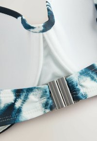 Fehér és kék batikolt mintájú melltartó, párnázott kosarakkal, hálós béléssel és ezüstszínű fém csattal hátul. Simító textil felület.