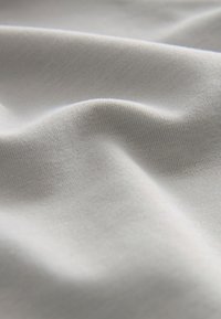 Tissu gris clair doux et lisse avec des plis subtils et une fine texture tricotée visible en gros plan.