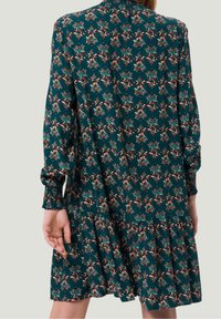 Vestido floral con fondo en tonos verde azulado, mangas largas, puños con fruncidos y un dobladillo en capas con un estampado botánico repetido en tonos de rosa y verde.