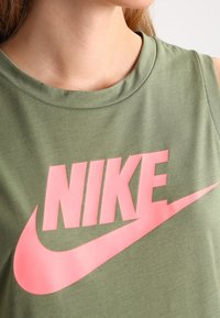 Grön ärmlös Nike-topp med en framträdande rosa logotyp på framsidan, tillverkad av en mjuk bomullsblandning.