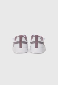 Vita sneakers med lila och turkosa prickiga ränder sedd från baksidan på en helt vit bakgrund.